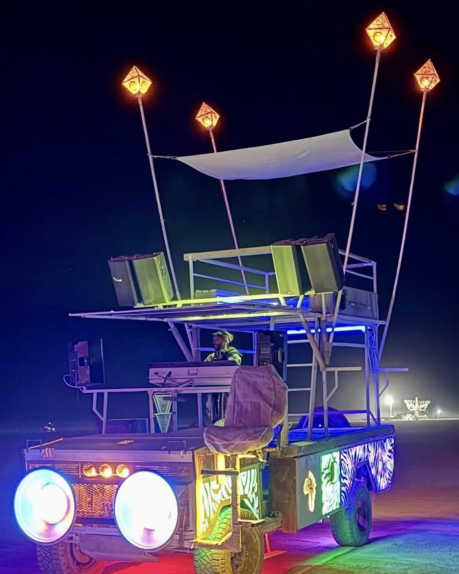 Rexan, the Sundowners art car, lit up at night on the playa with a DJ on the upper deck